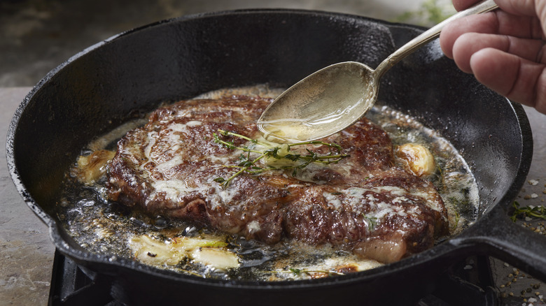 a nicely browned steak being basted with butter in a pan