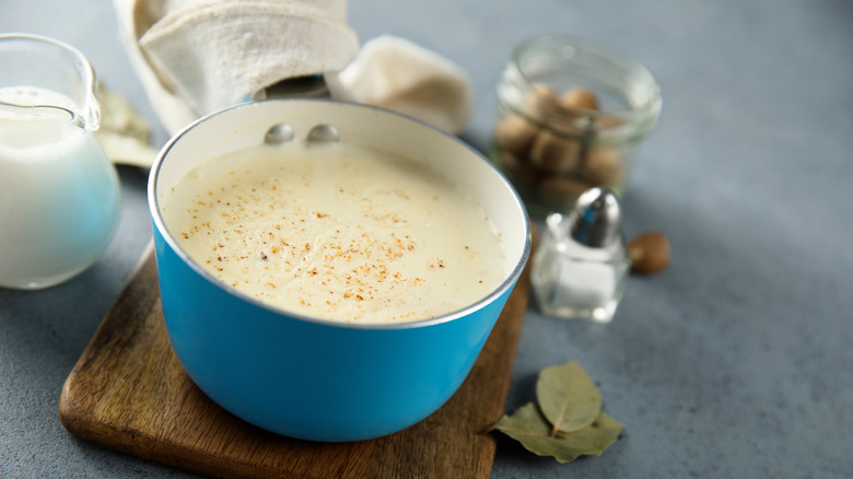 A blue pot containing bechamel sauce with nutmeg sprinkled on top