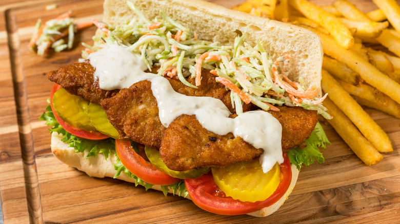 an open fried fish po boy sandwich with tartar sauce on a wooden cutting board with french fries