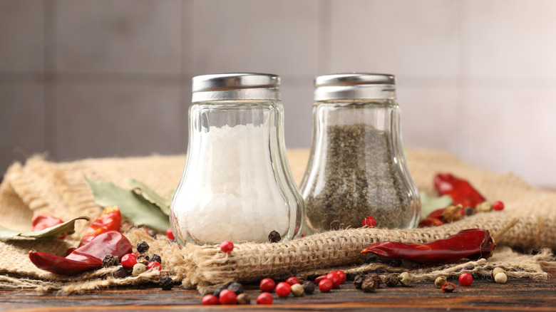 Salt and pepper shakers sit in a table with dried peppercorns.