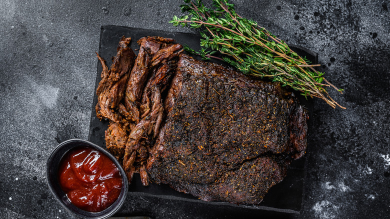 Texas-style brisket is sliced on a plate with  herbs and BBQ sauce.