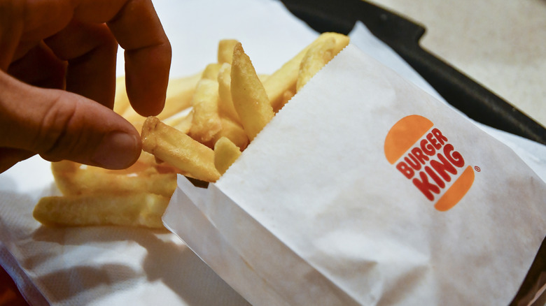 A hand reaches for a Burger King French fry.