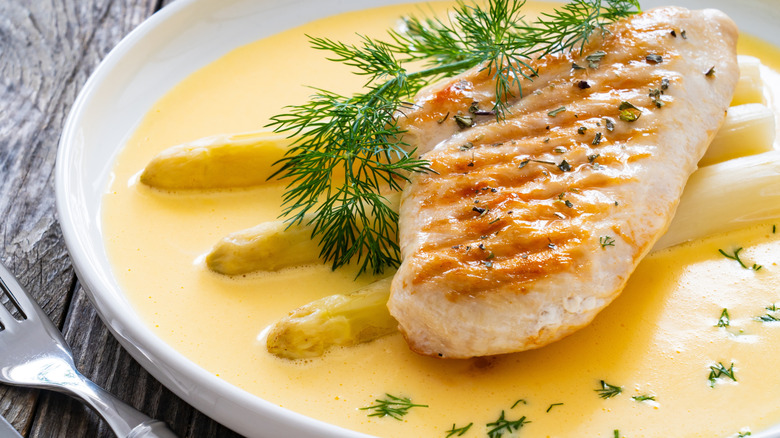 Seared chicken breast served over white asparagus spears on top of pool of hollandaise sauce