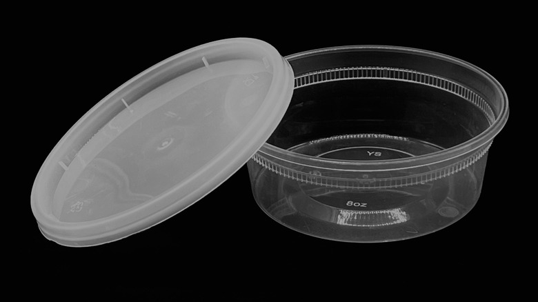 An empty plastic deli container with lid askew on a black background