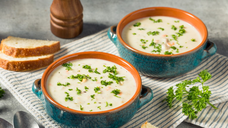 bowls of garnished clam chowder with bread and striped napkin