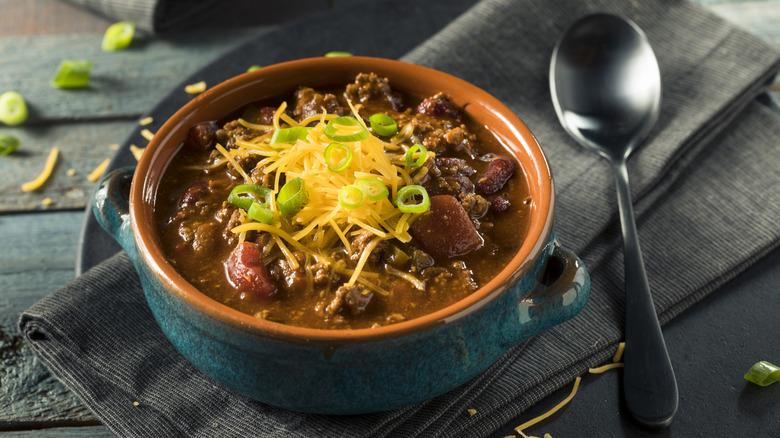 Green bowl of beef chili topped with cheese and green onions