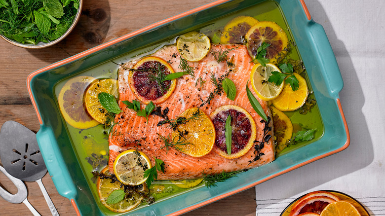 slow roasted salmon in a turquoise baking dish with citrus, olive oil, and herbs