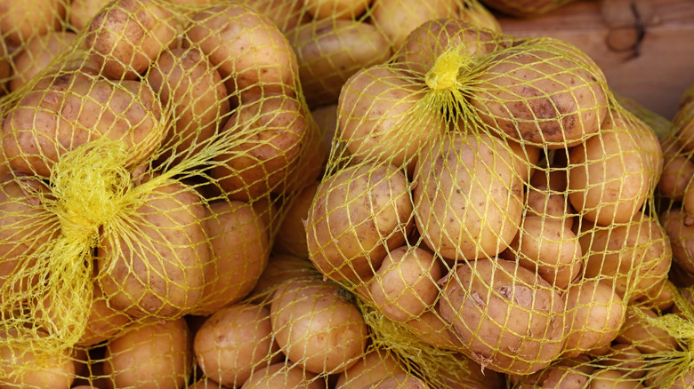 Yellow netted bags of whole white potatoes in a pile