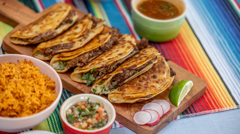 Birria tacos on a wood board with consomé
