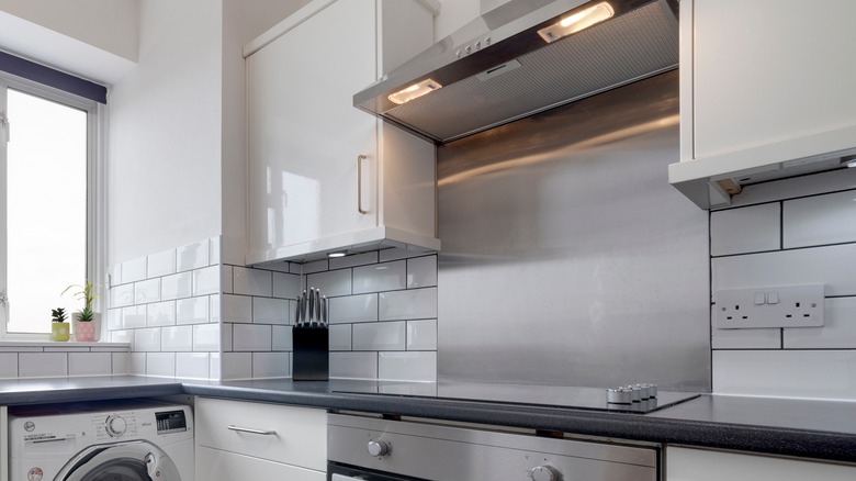 A white kitchen with a silver backsplash behind the cooktop