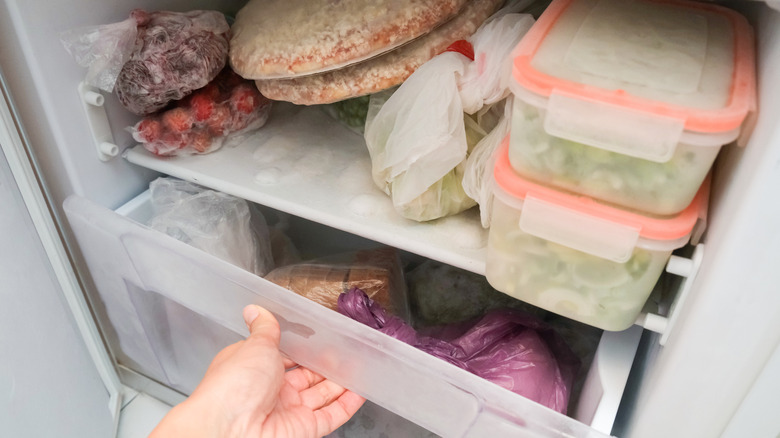 A hand opens a drawer in a freezer full of food.