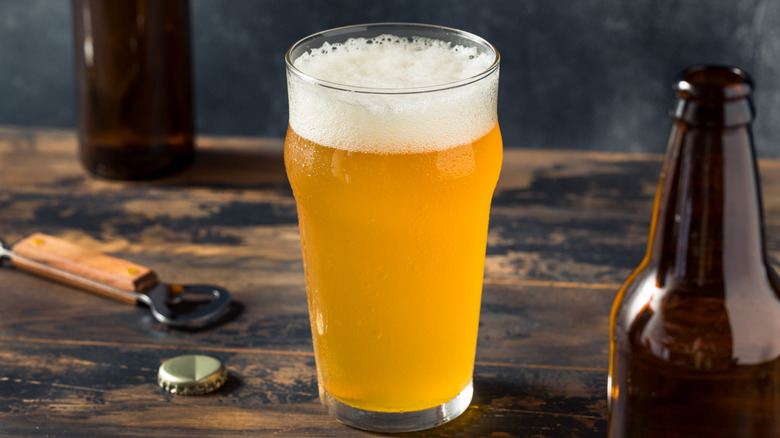 Farmhouse ale beer in glass next to bottles and opener