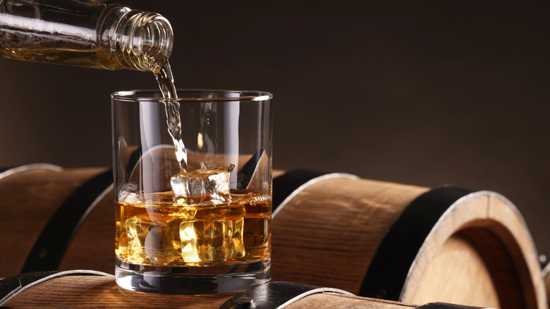 A glass of bourbon on the rocks on a barrel