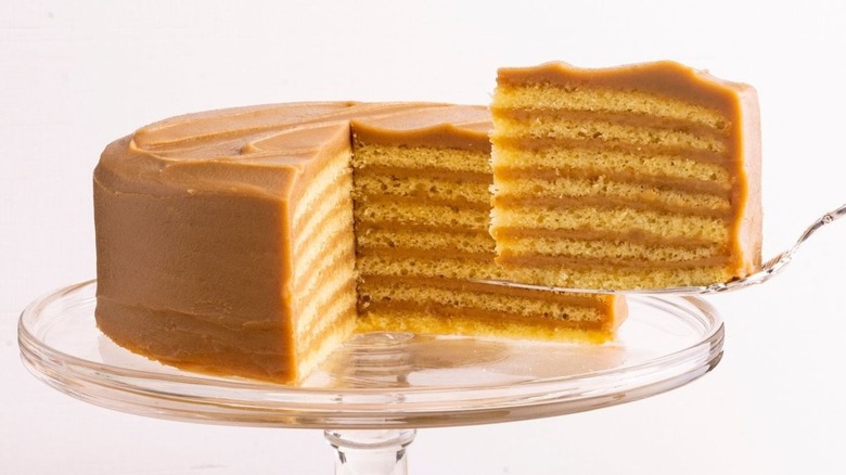 The 7-Layer Caramel Cake from Caroline's Cakes on a clear platter with a serving knife