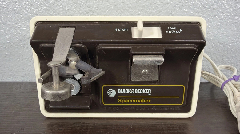 A brown and white Black & Decker Spacemaker can opener featuring a switch to start and unload sitting on a table top