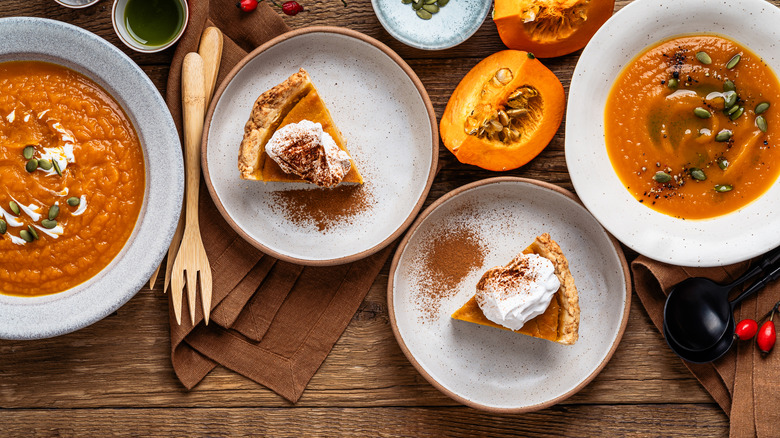 Pumpkin pie and pumpkin soup with quartered pumpkin and other garnishes on a table.
