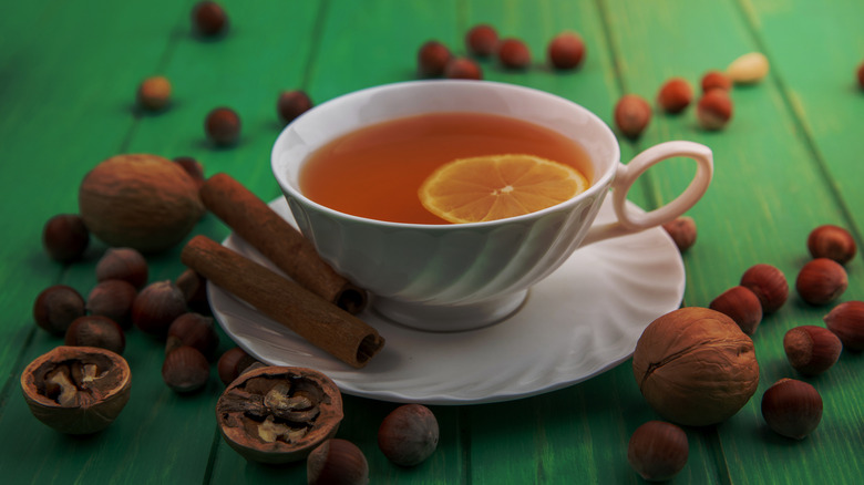 Hot toddy in teacup with nuts, cinnamon sticks