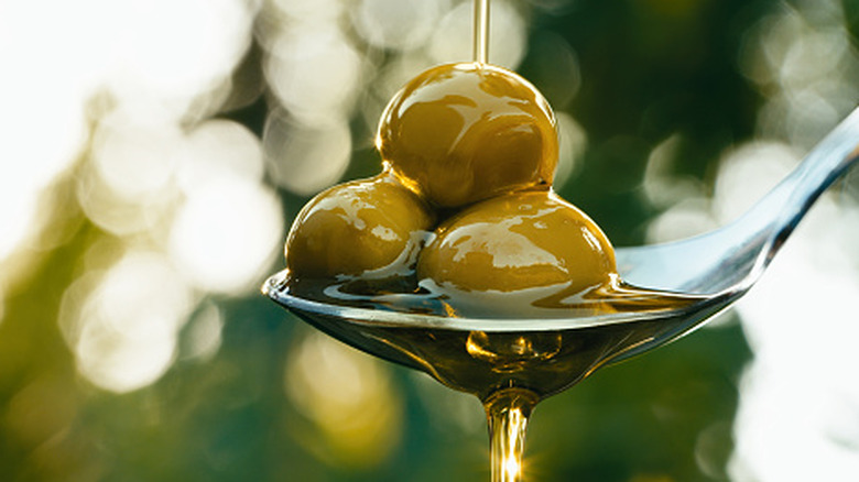 Olive oil being poured over a spoonful of green olives.