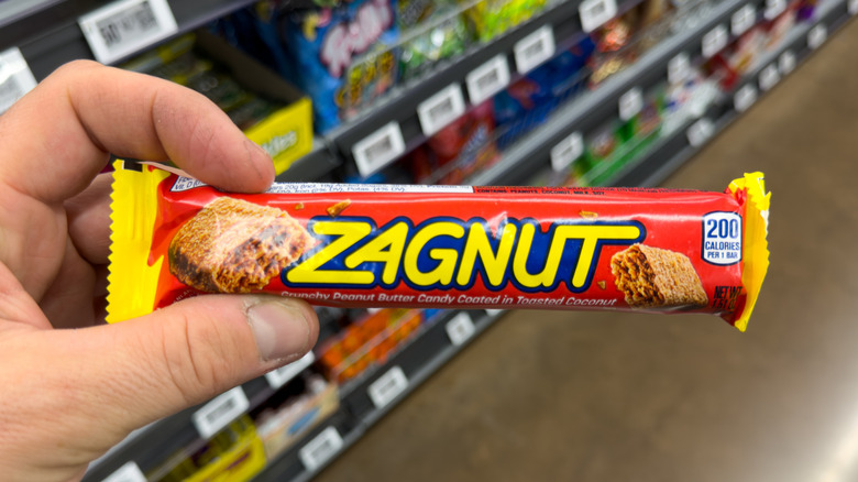 a hand holding a Zagnut candy bar in a grocery store