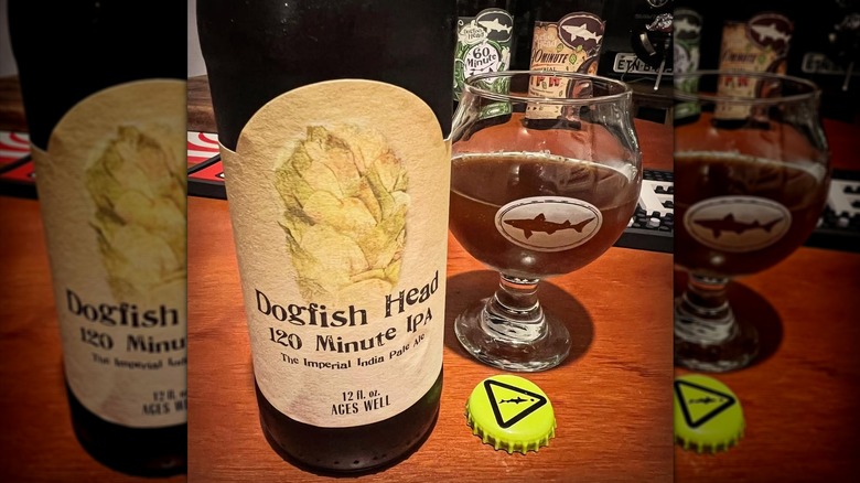 Dogfish Head 120 minute IPA bottle and half-filled glass of beer. Other Dogfish Head beer bottles visible in background