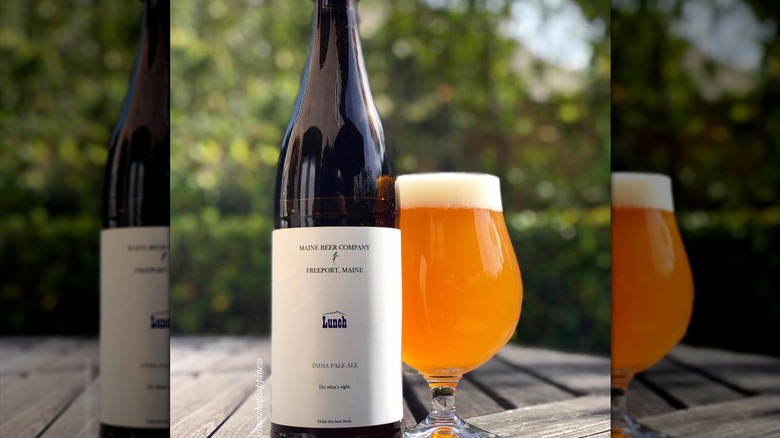 Bottle of Lunch IPA next to a fully beer glass on a weathered outdoor wooden table