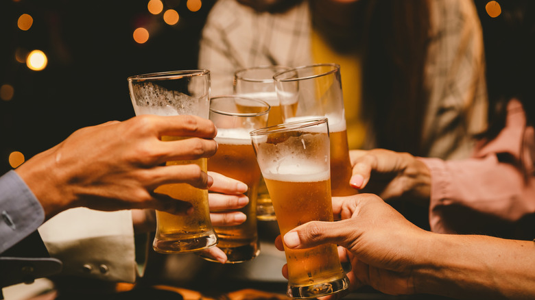 Five people, unseen, toasting with pint glasses of beer.