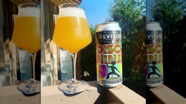 A can of Disco Ninja IPA next to a filled long-stemmed beer glass on the railing of a deck.