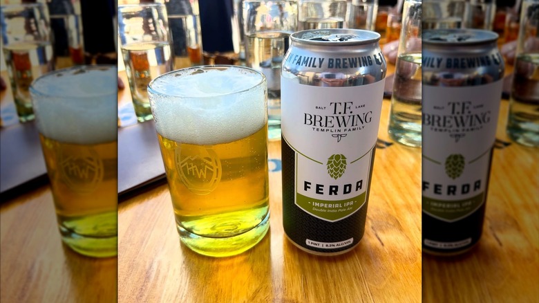 Glass of foamy beer next to a Ferda IPA can.