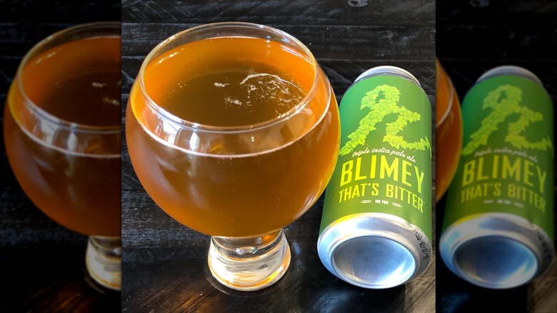 Filled globe glass of IPA next to a can of Blimey That's Bitter IPA.