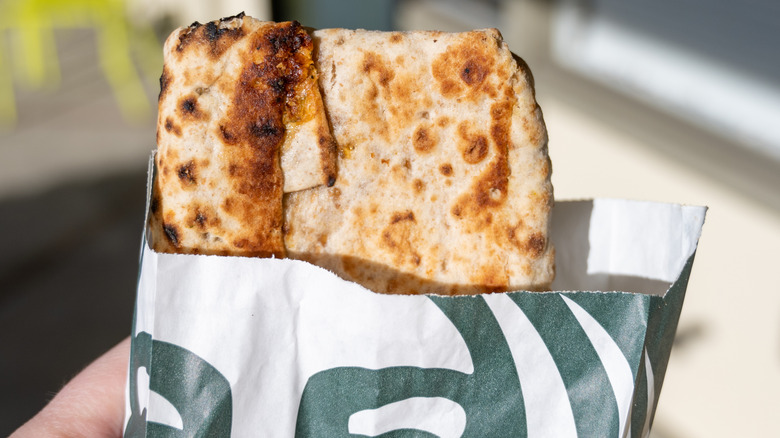 hand holding a spinach and feta wrap in a paper bag from Starbucks