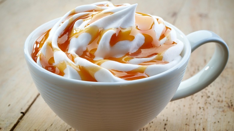 A whipped cream and caramel topped latte in a white mug