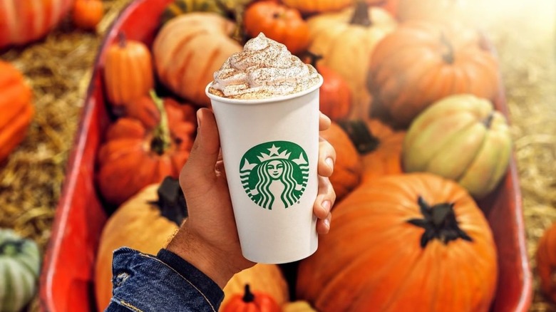 hand holds Starbucks PSL, pumpkin patch
