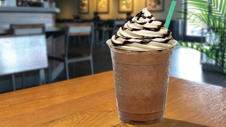 An iced mocha with whipped cream, chocolate drizzle, and a green straw on a table