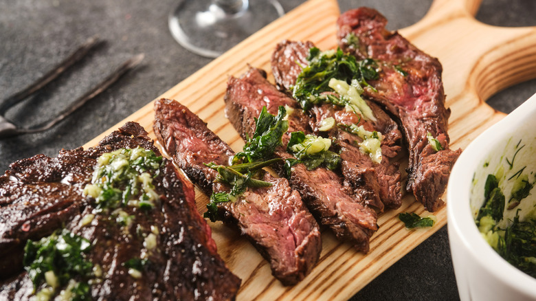 Sliced hanger steak with chimichurri on wooden serving board