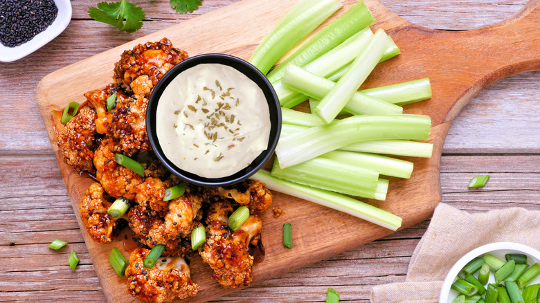 Buffalo style cauliflower with celery and dip on a cutting board