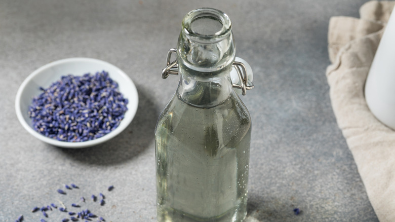 Glass bottle of simple syrup with white bowl of lavender blossoms in background