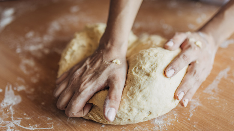 Hands kneading bread dough on a floured wooden surface