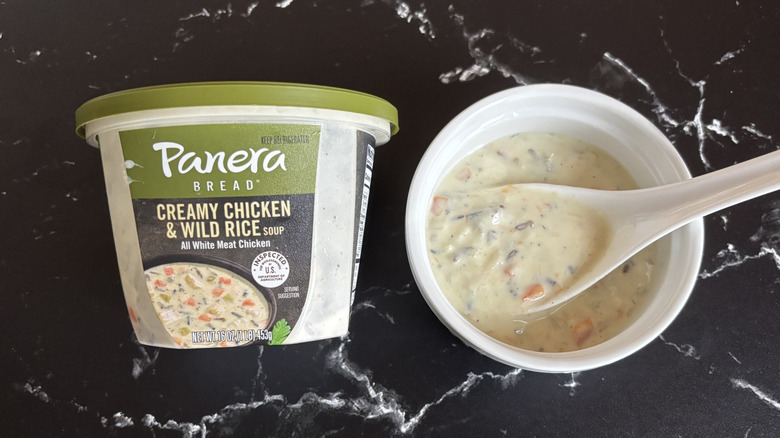 a bowl of Panera Creamy Chicken and Wild Rice Soup beside the container it came in