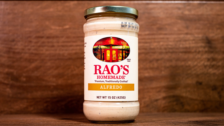 A jar of Rao's Alfredo sauce sits on a wood shelf.