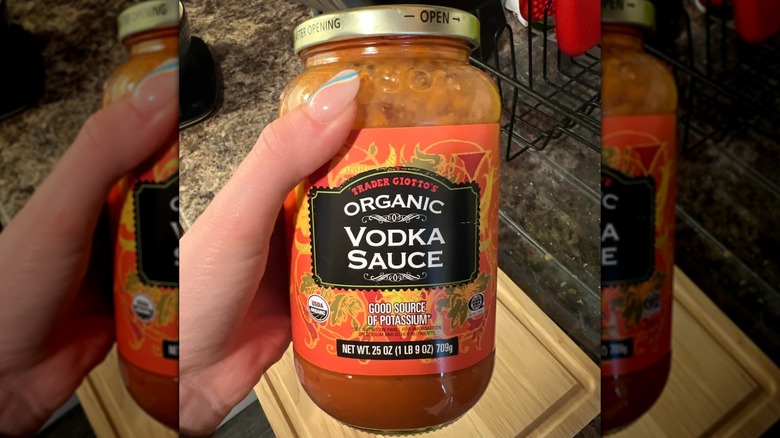 A hand holds a can of Trader Joe's Organic Vodka sauce over a wooden cutting board on a kitchen counter.