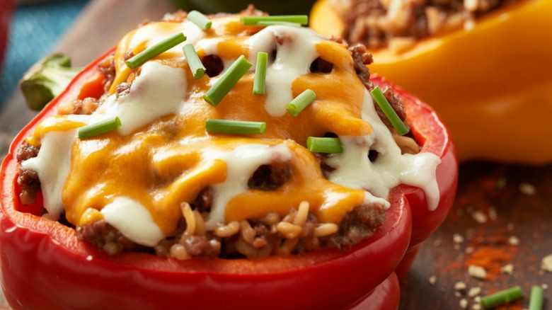 A close-up of a red stuffed bell pepper topped with melted cheese and chives