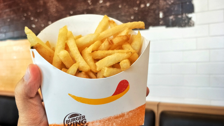 A hand holding up a order of Burger King fries