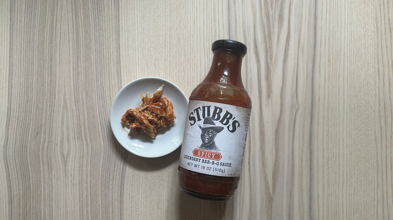 bottle of Stubb's Spicy BBQ sauce is next to a bowl of pulled pork.