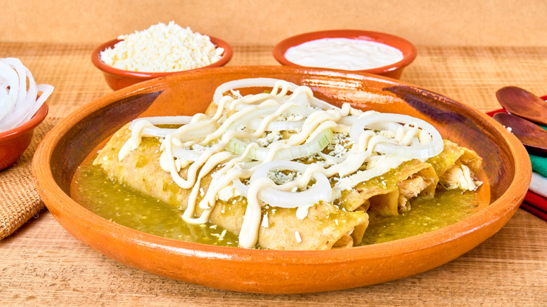 four enchiladas covered in a light green sauce and cheese in orange dish with ramkens
