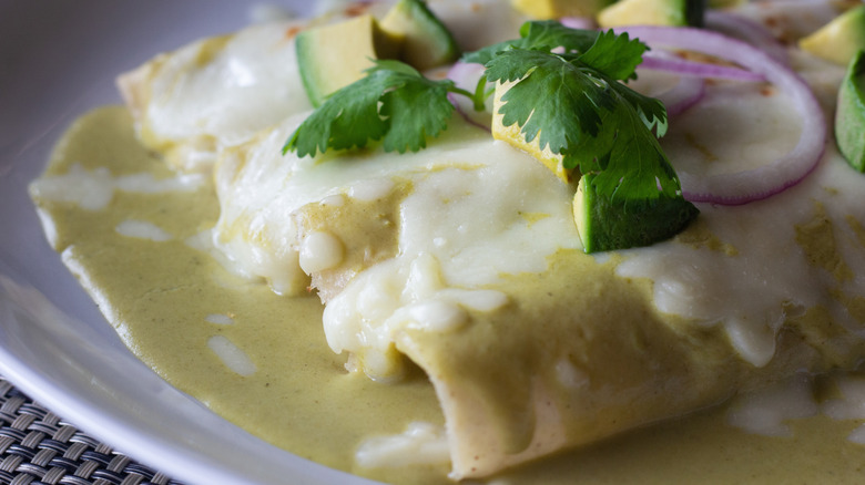 A close-up of Swiss enchiladas covered in cheese and sauce with cilantro and onion and avocado garnish