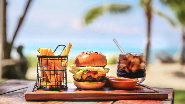 burger fries and drink at beach with palm trees