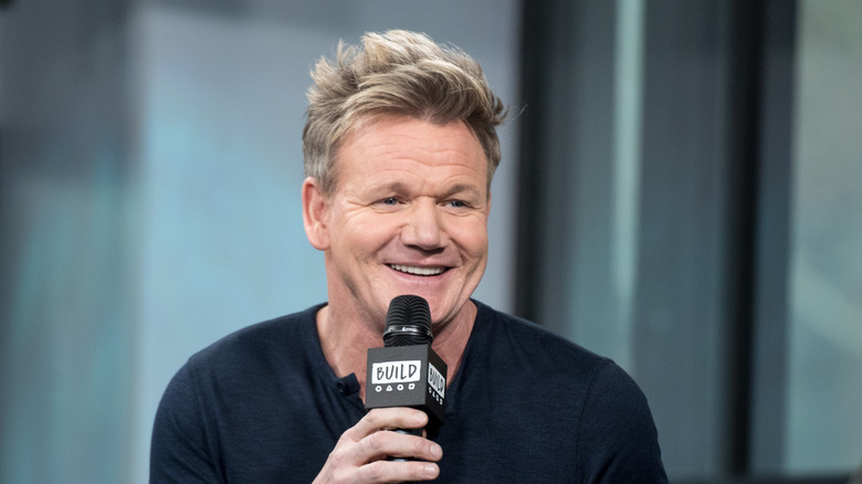 Gordon Ramsay in a dark sweater holding a microphone