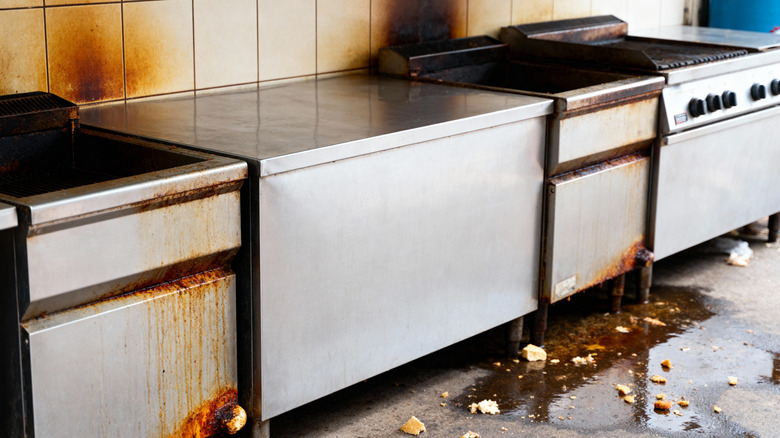 A dirty commercial kitchen with grease on the floor in the front of the fryers