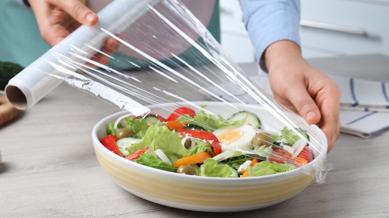 Hands wrapping a bowl of salad with plastic wrap