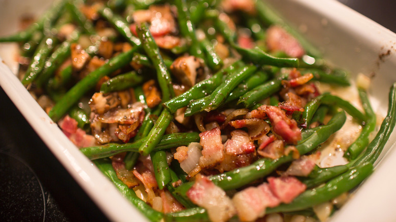 Chopped green beans with pieces of bacon inside white casserole dish